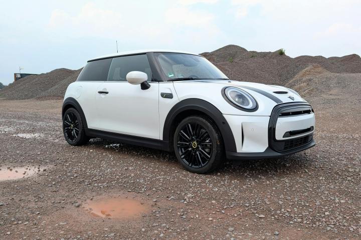 White compact car parked on gravel with hills in the background.